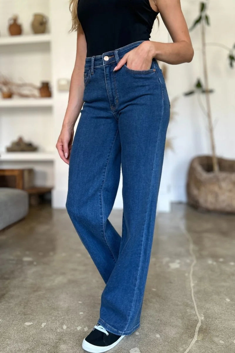 Dark wash wide-leg jeans with a high waist and white laces on black sneakers.