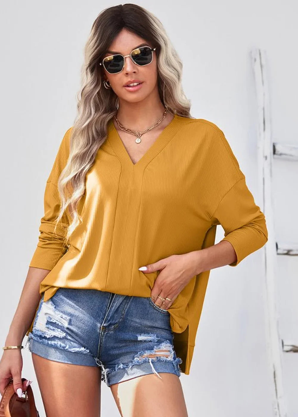 Yellow ribbed V-neck long-sleeve top on model with distressed denim shorts and gold jewelry.