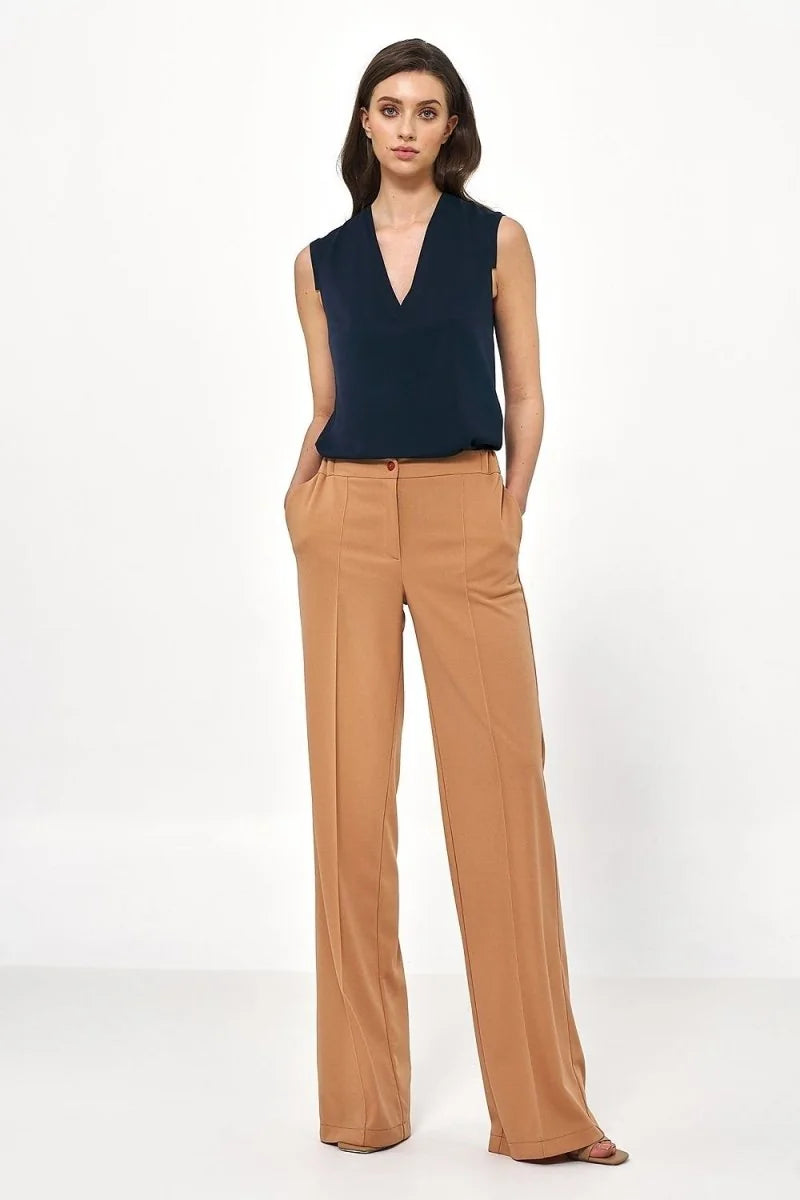 Full-length shot of a woman wearing relaxed-fit, camel-colored wide-leg trousers with a v-neck navy blue sleeveless top.