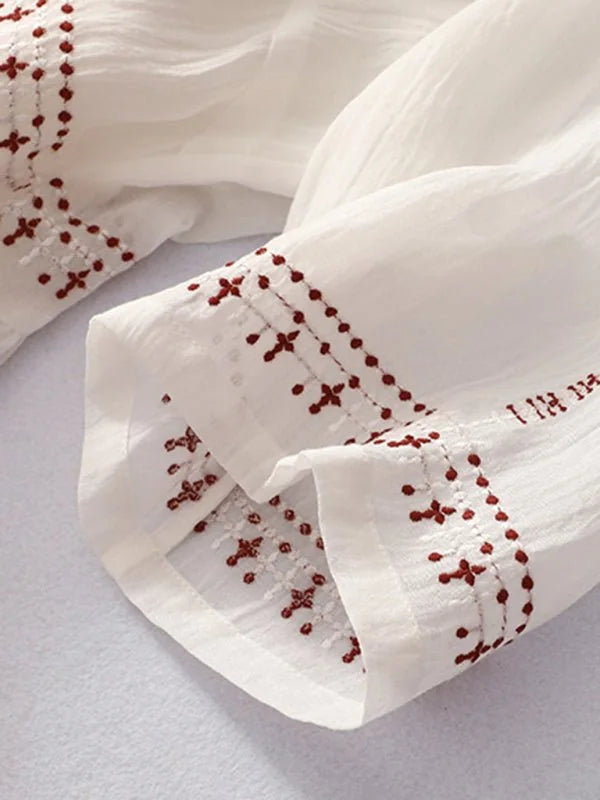 Close-up of white linen-blend dress with red embroidered floral accents on the cuffs.