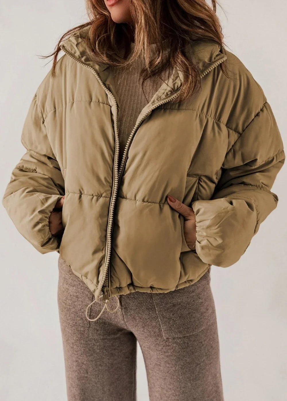 Tan puffer jacket with zipper closure and drawstring hem, worn by a model.