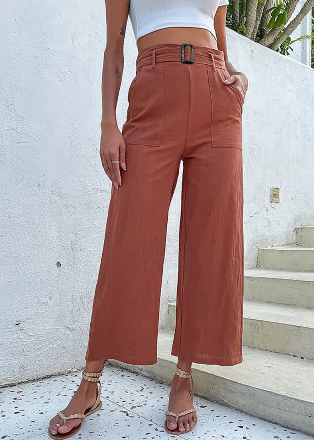 Rust-colored wide-leg pants with a belted waist and pockets, shown on a model with sandals.
