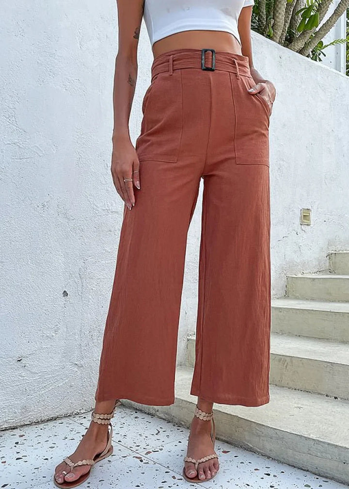 Rust-colored wide-leg pants with a belted waist and pockets, shown on a model with sandals.