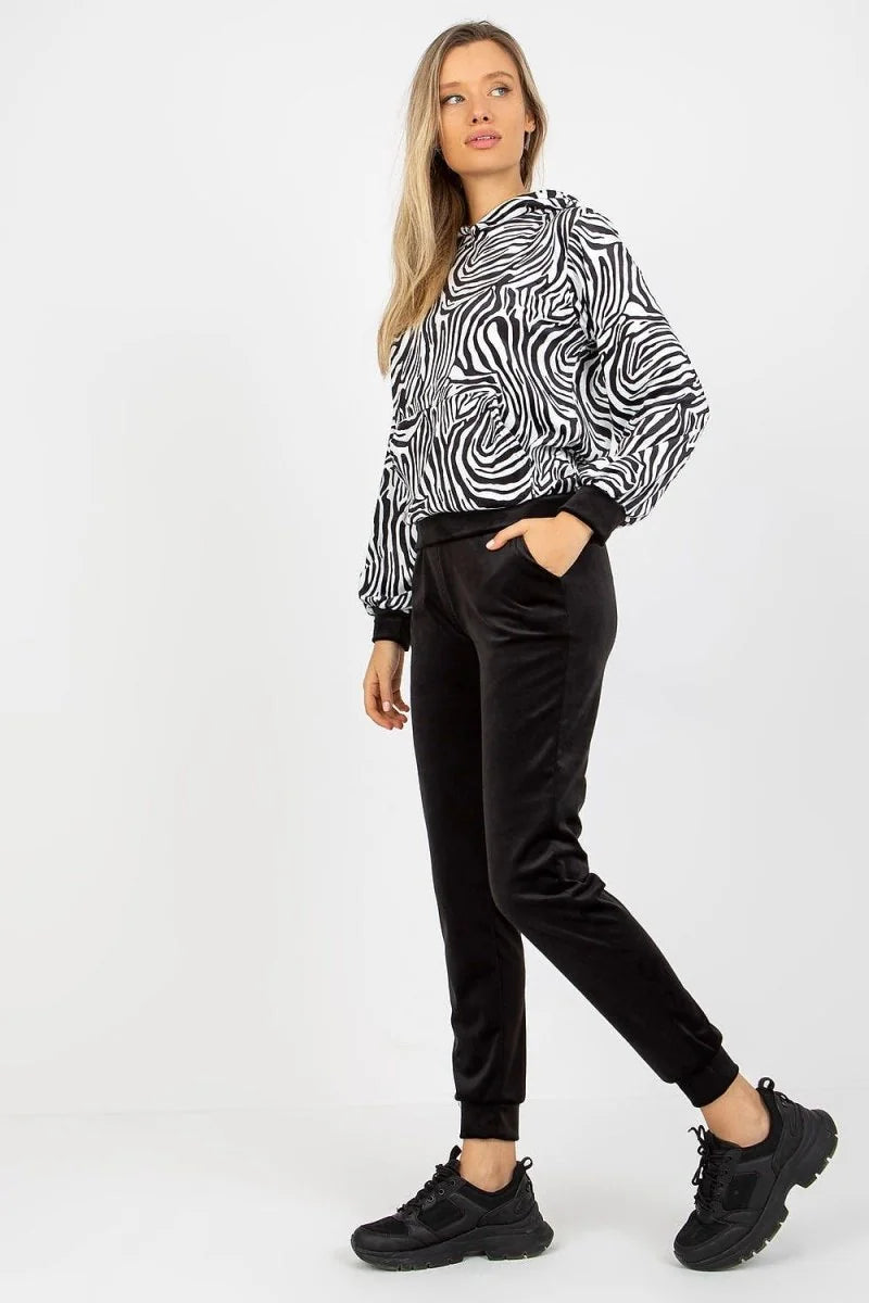 Woman in black velvet joggers with a black and white zebra print hoodie and black sneakers.