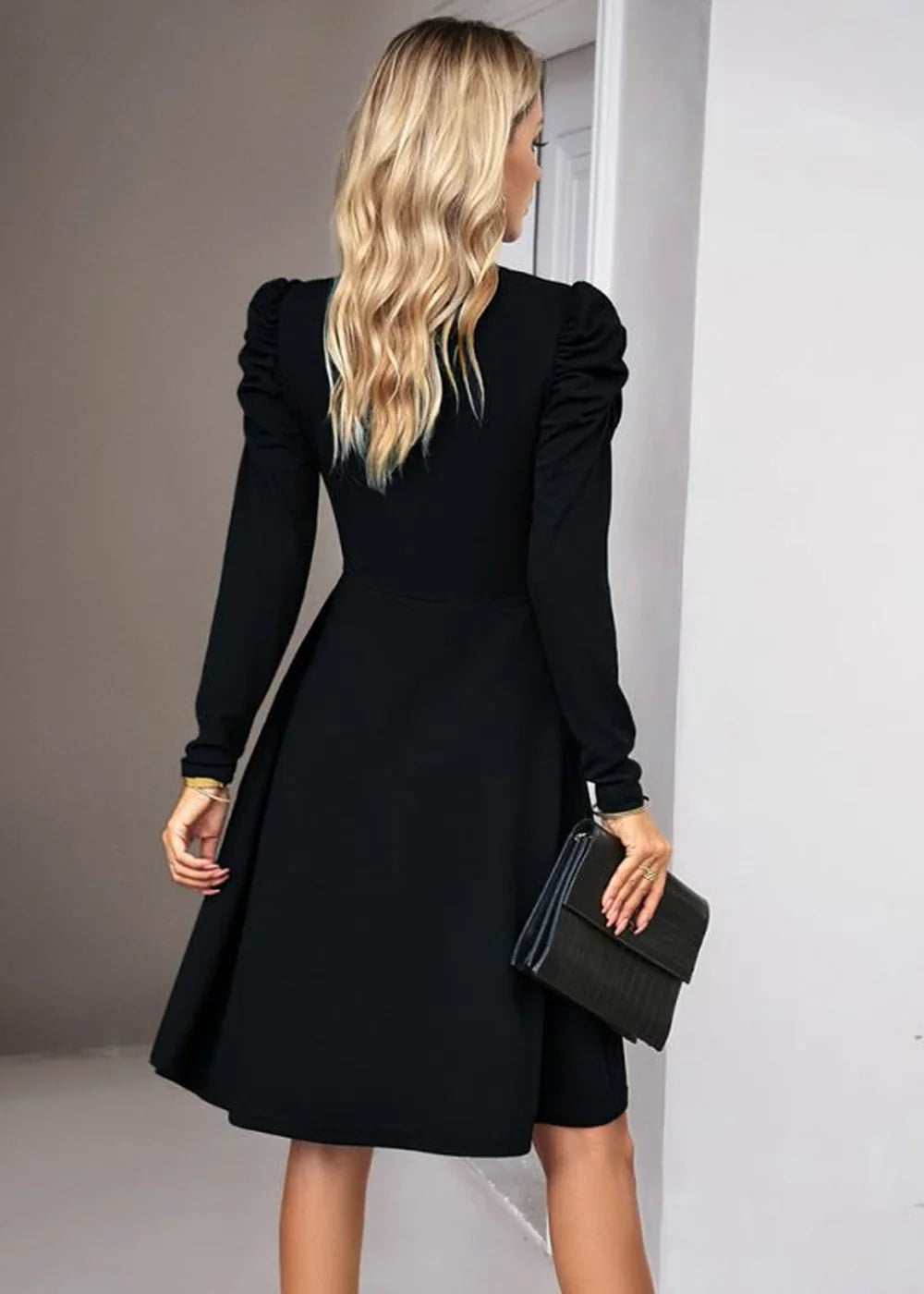 Black long-sleeve dress with puff sleeves and a flared skirt, shown from the back with a clutch.