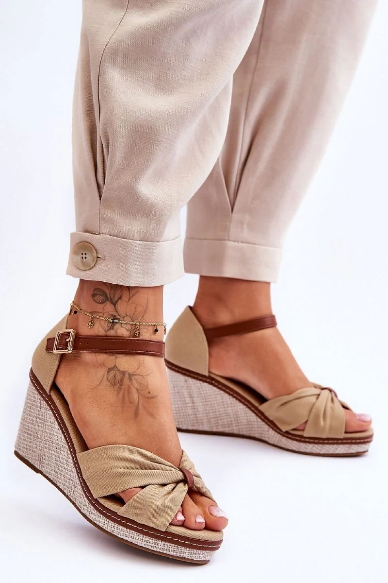 Beige fabric wedge sandals with knotted toe and brown ankle strap, on a model.
