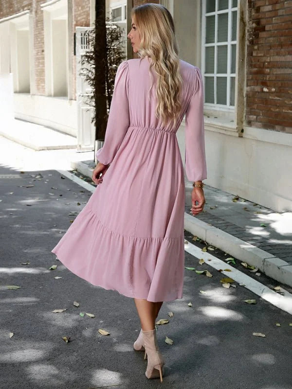 Light pink polyester midi dress with ruffled hem, cinched waist, and long sleeves, worn by a woman from behind.