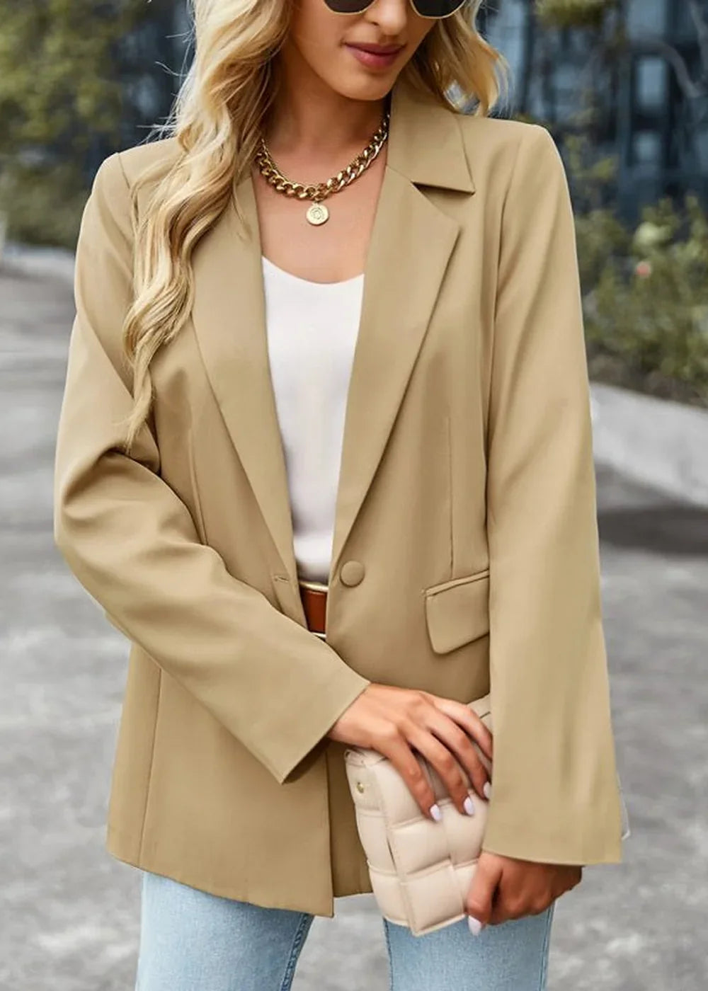 Woman in a tan polyester blazer with a gold chain necklace and a quilted clutch.