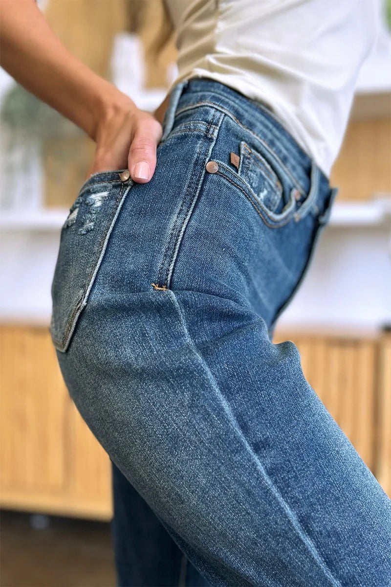 Close-up of distressed medium wash denim jeans with bronze button details and a distressed pocket.