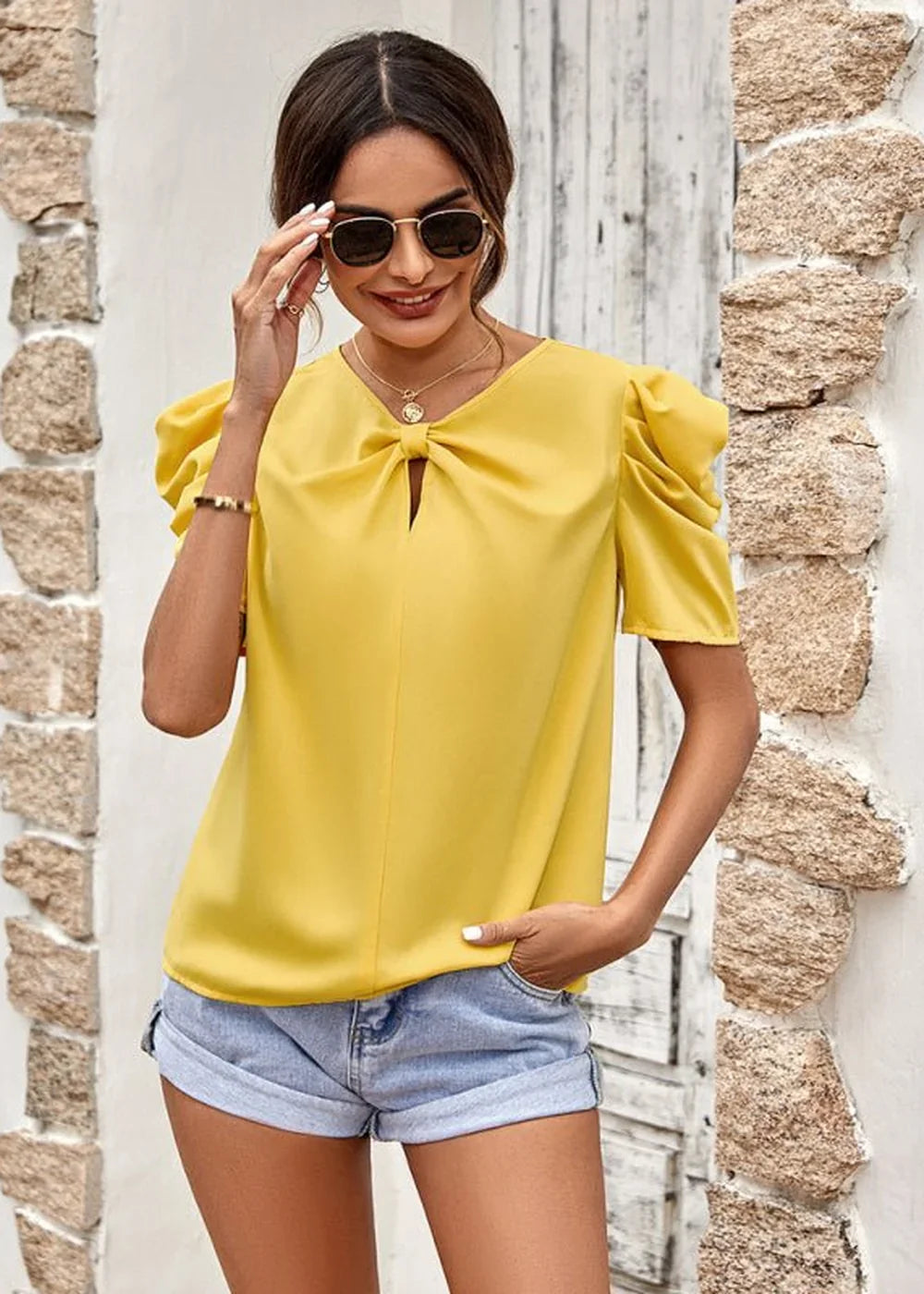 Woman in yellow puff-sleeve top with keyhole cutout and denim shorts.