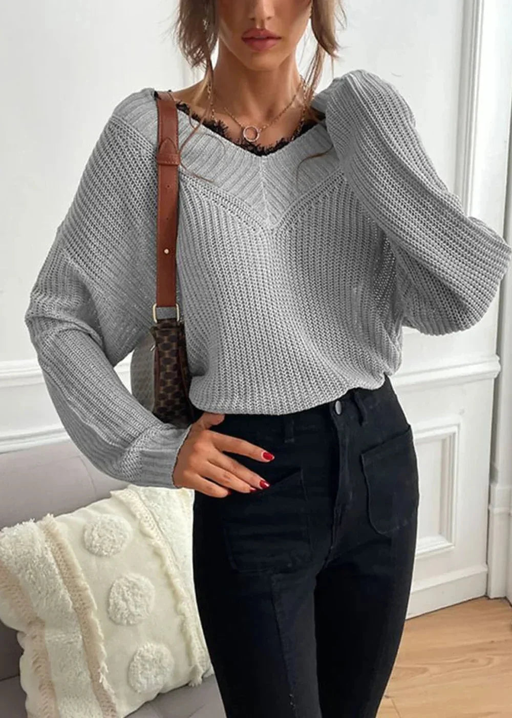 Grey knit v-neck sweater with black lace trim, worn by a model with black jeans and a brown shoulder bag.