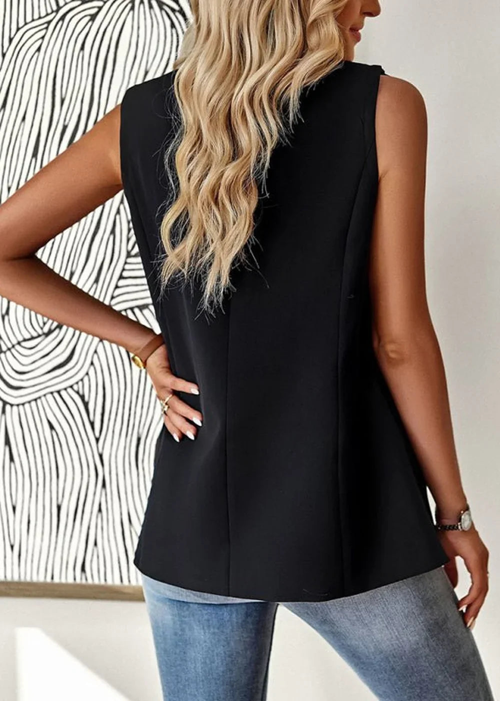 Back view of a black sleeveless blazer on a model wearing blue jeans.