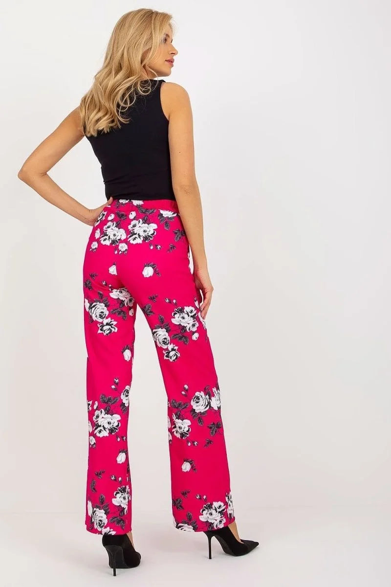Model in vibrant pink wide-leg pants with a black and white floral print, paired with a black top.
