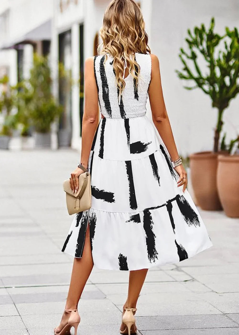 Woman from behind wearing a white tiered dress with black abstract brushstroke print and nude heels.