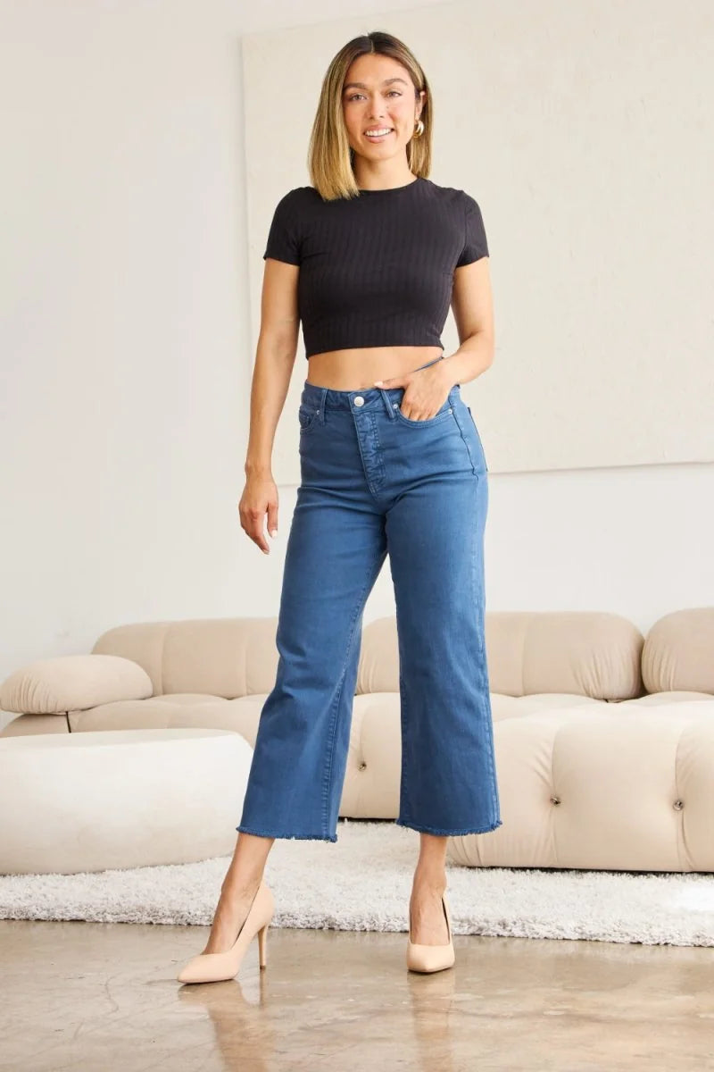 Woman in a black crop top and blue wide-leg jeans with frayed hem, wearing nude pumps.