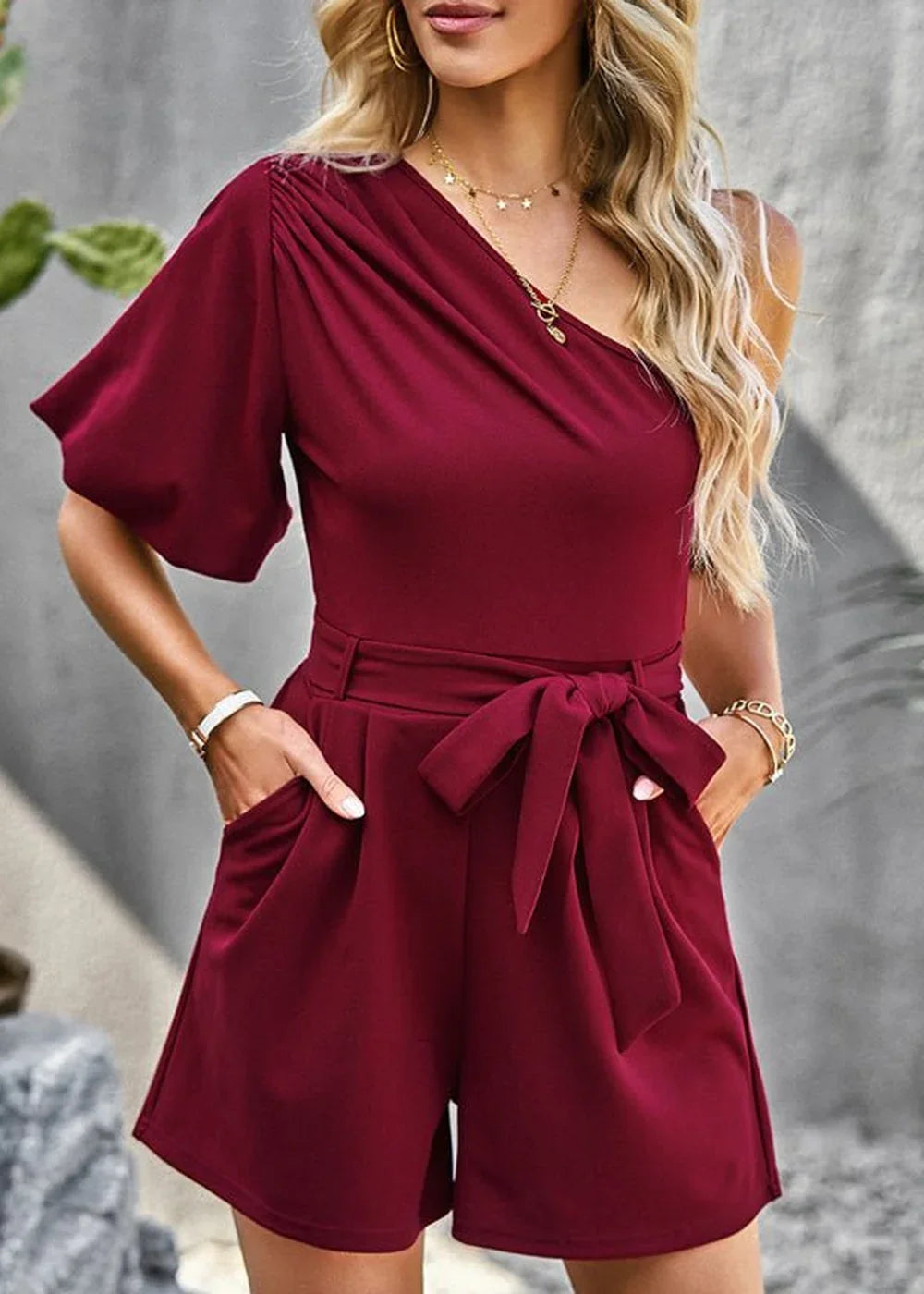 Maroon one-shoulder romper with puff sleeves, self-tie waist, and pockets on model.