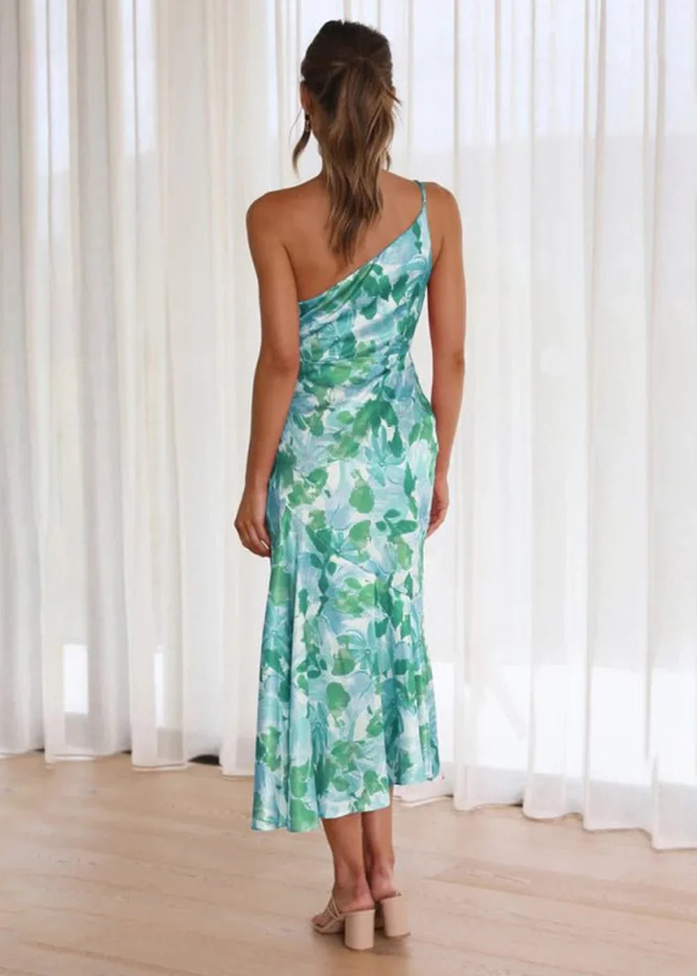 Woman in a one-shoulder midi dress with a green and blue floral print.