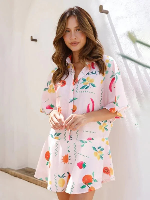 Pink jumpsuit with a playful fruit and chili pepper print, short sleeves, and a flared skirt.