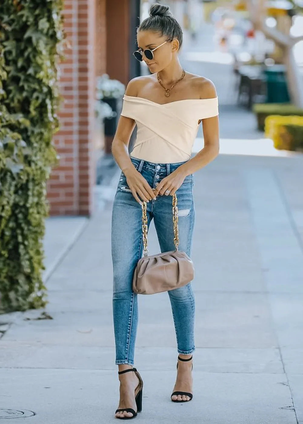 Off-the-shoulder cream wrap top with gold chain purse and ripped jeans on model