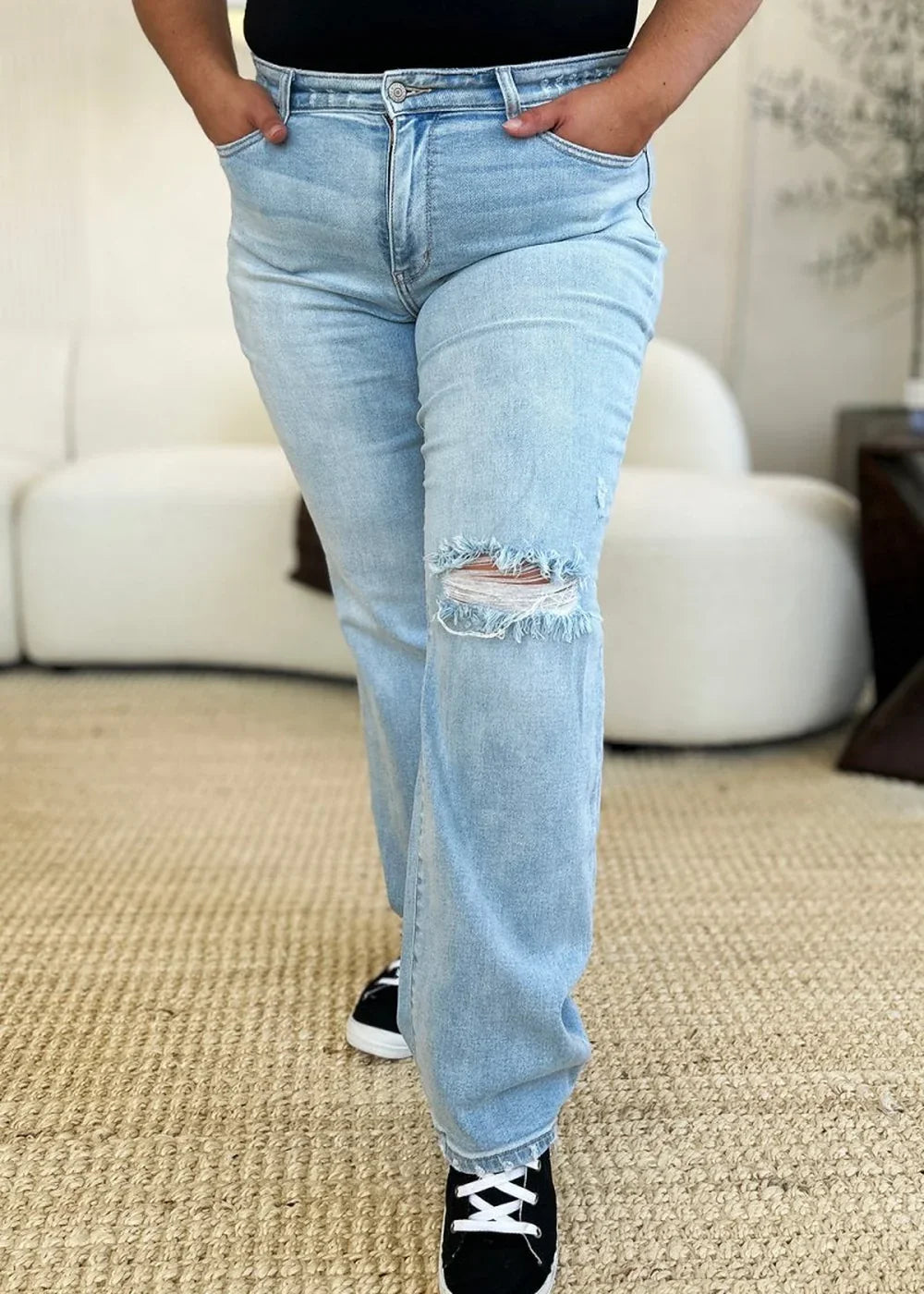 Light wash distressed denim jeans with frayed knee detail and black lace-up sneakers.
