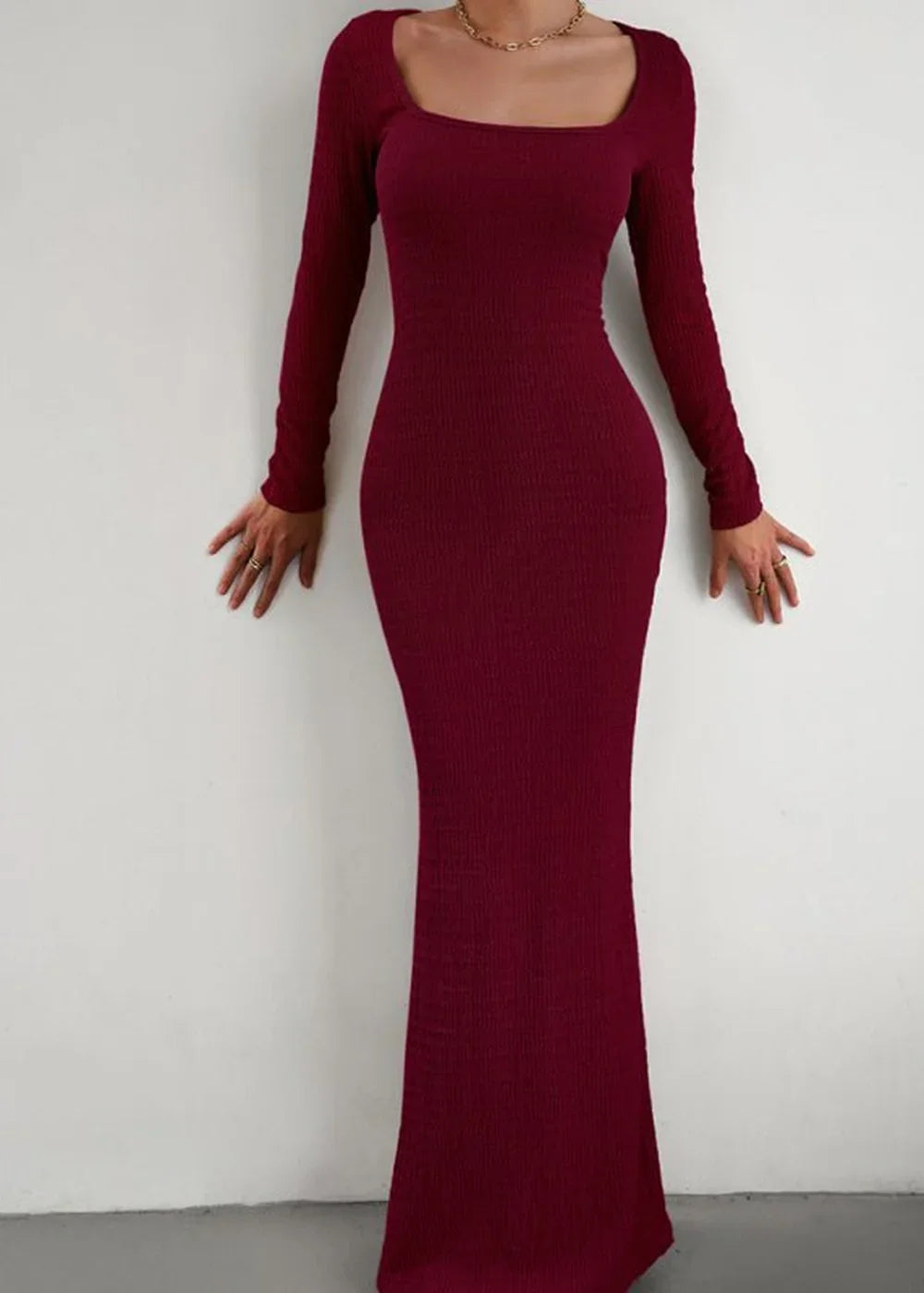 Long-sleeved burgundy ribbed maxi dress with a square neckline, fitted silhouette, and gold jewelry.