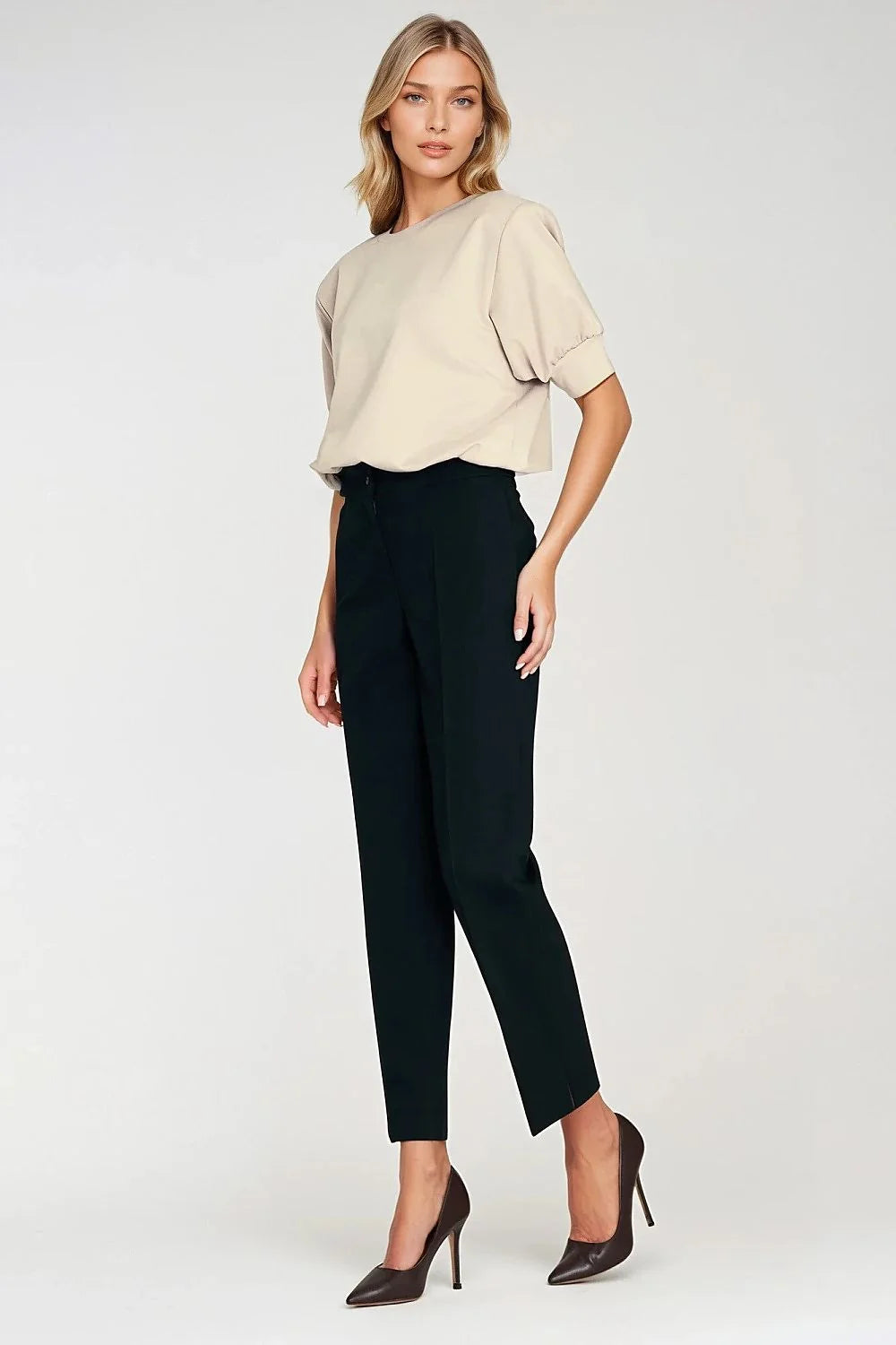 Woman in oversized beige top and black pants with pointed-toe heels.