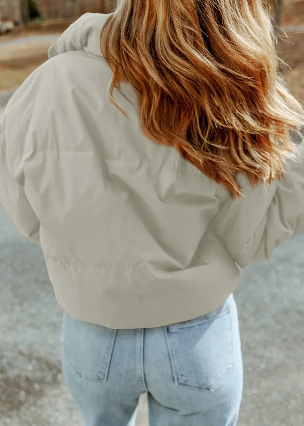 Back view of a woman wearing a light beige puffer jacket and light wash jeans.