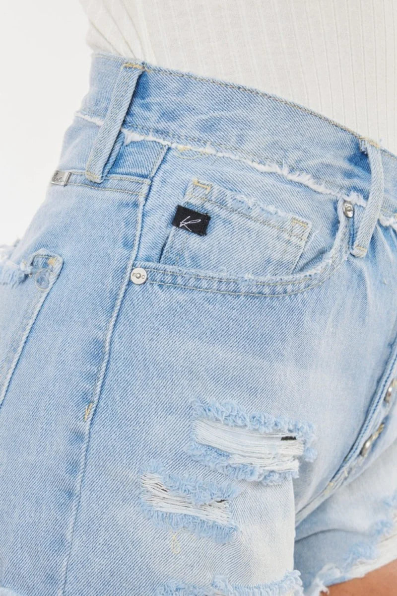Close-up of light wash distressed denim shorts with frayed hem and black brand tag.