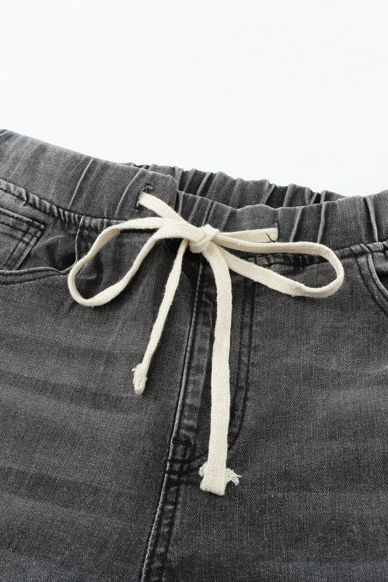 Close-up of grey distressed denim pants with a drawstring waist and frayed hem.