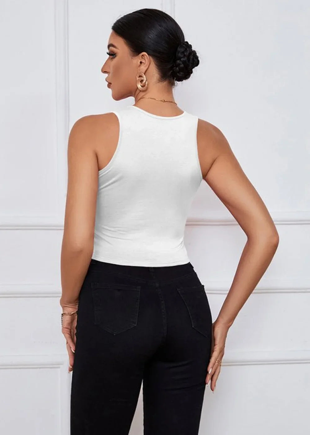 Back view of a woman wearing a white sleeveless cropped top and black skinny jeans.