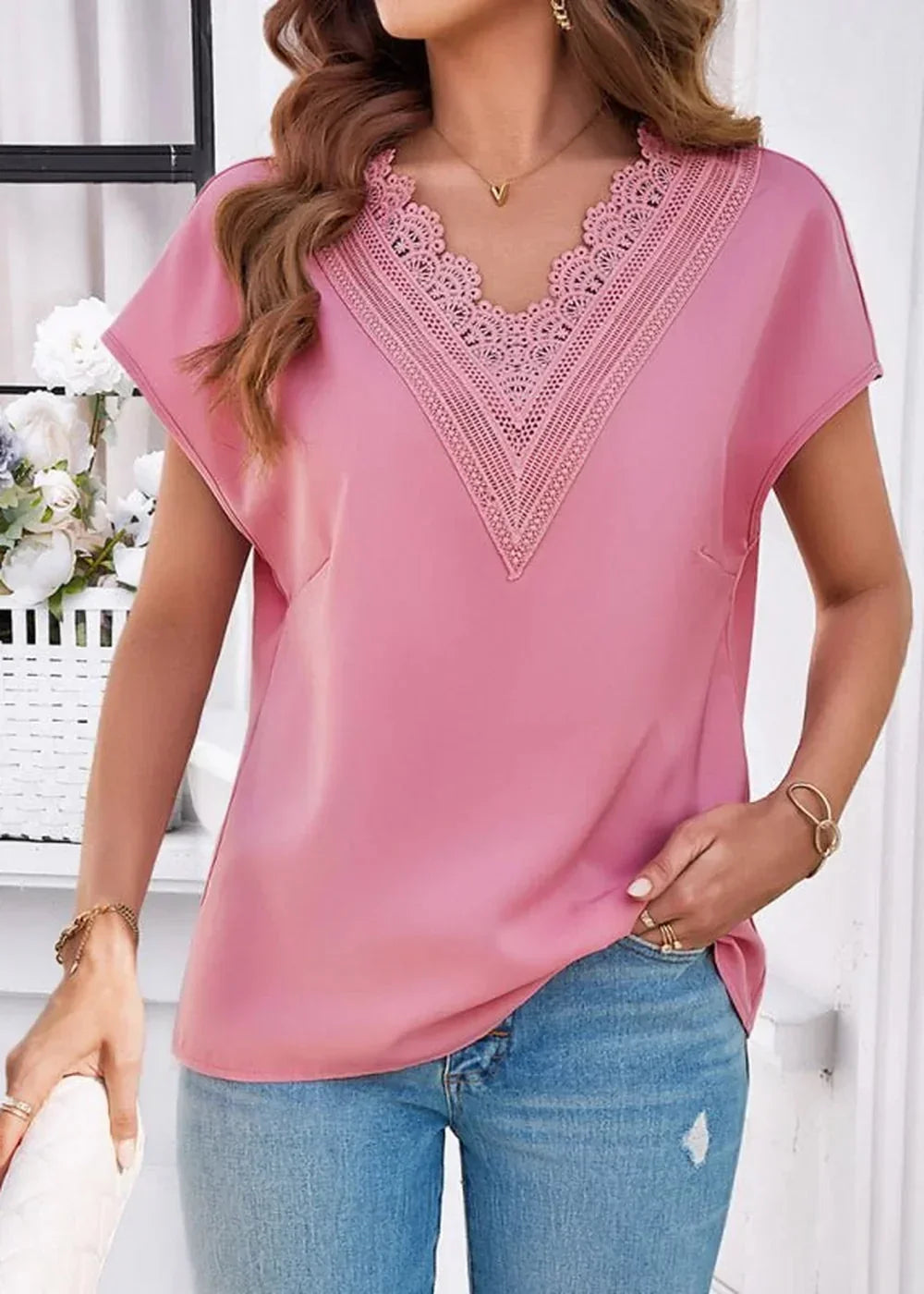Pink v-neck top with lace trim and short sleeves, paired with distressed blue jeans.