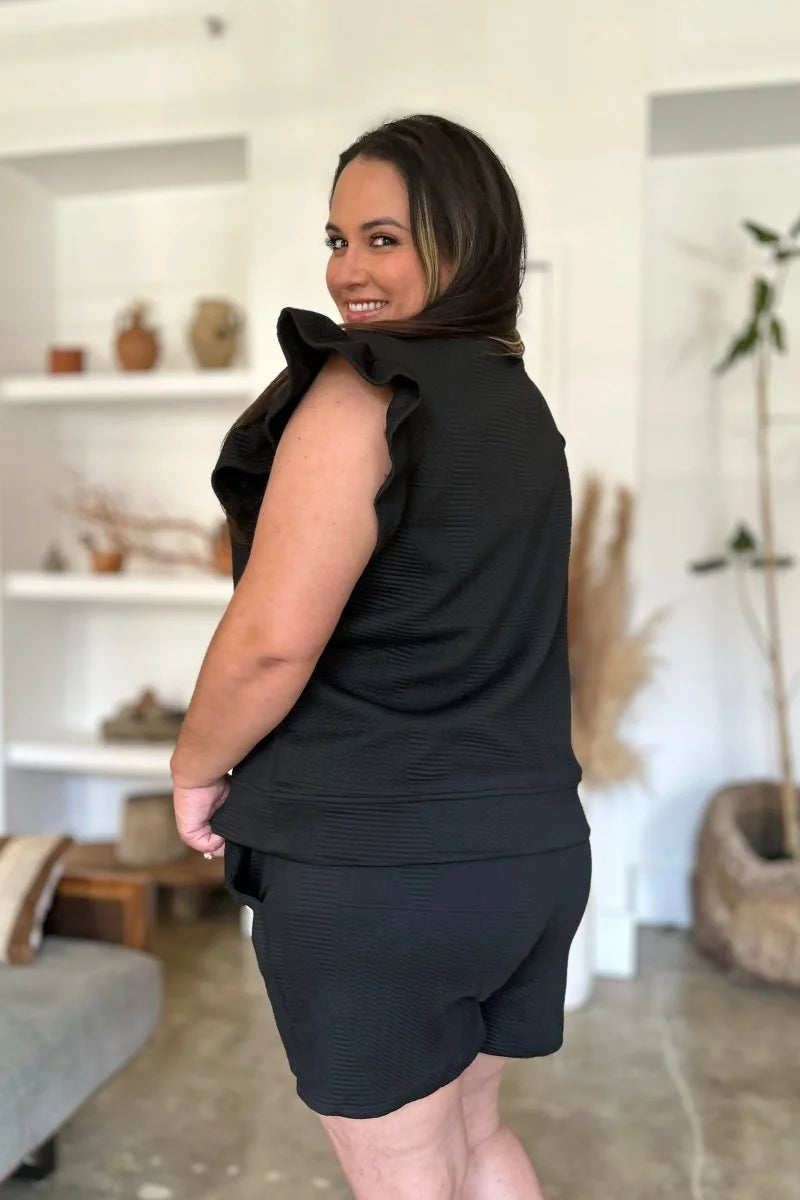 Black textured short suit with ruffled sleeves, shown from the back on a model.