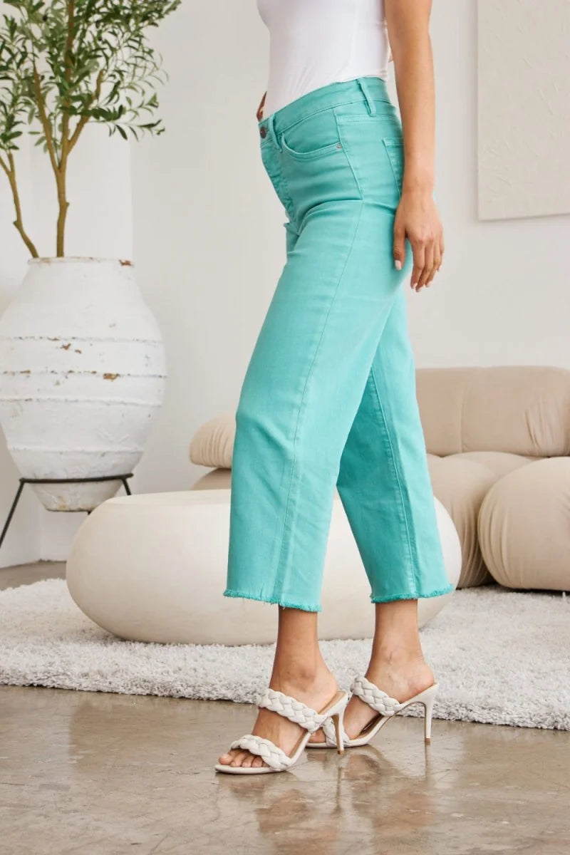 Teal cropped jeans with frayed hem, on model wearing white braided heels.