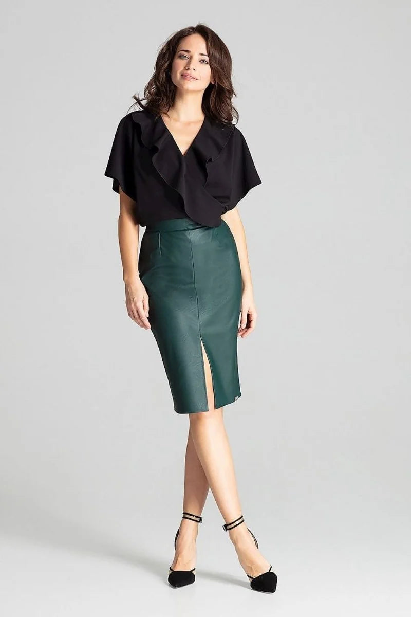 Full-length shot of a woman wearing a black ruffled v-neck top and a dark green faux leather pencil skirt with a thigh-hig...