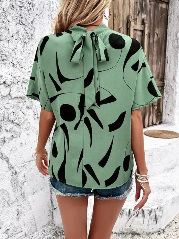 Back view of a light green top with a black abstract print and a bow tie detail at the neck.