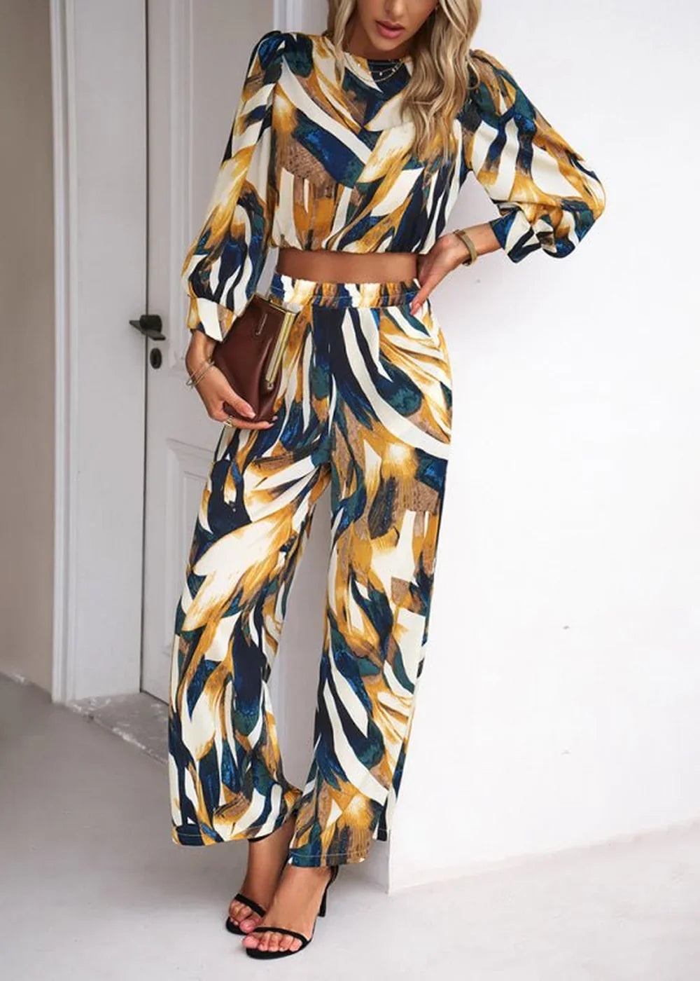 Woman in a cropped long-sleeve top and wide-leg pants with a bold abstract print in navy, gold, and white.