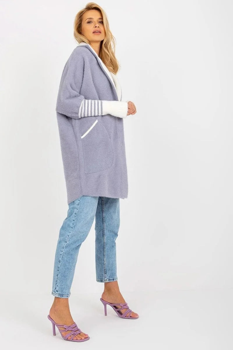 A woman wears a light purple, fuzzy cardigan with white striped cuffs and light wash jeans.