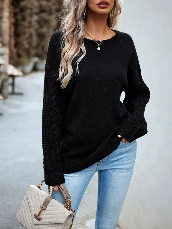 Black cable knit sleeve sweater with crew neck, paired with light wash jeans and a quilted handbag.