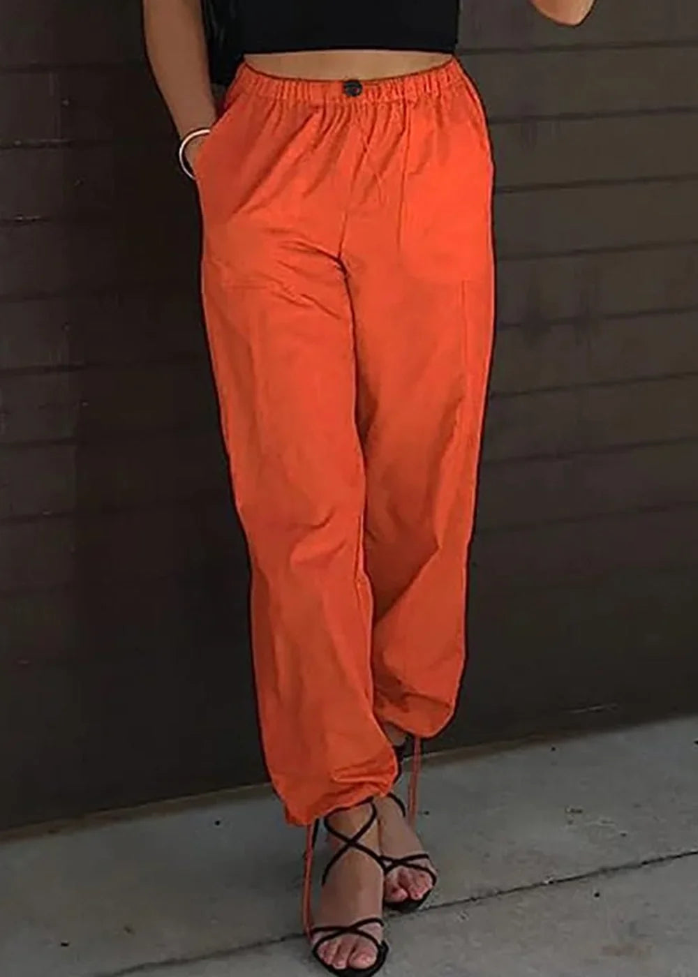 Orange high-waisted cargo pants with drawstring ankles and tie-up black heels on a model.