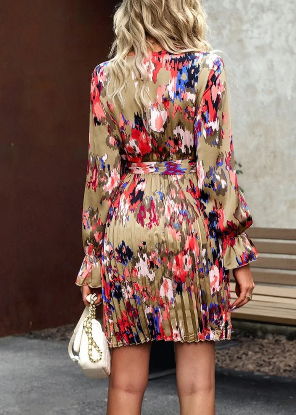 Khaki dress with colorful abstract floral print, long sleeves, and pleated skirt, held by a woman with a white purse.