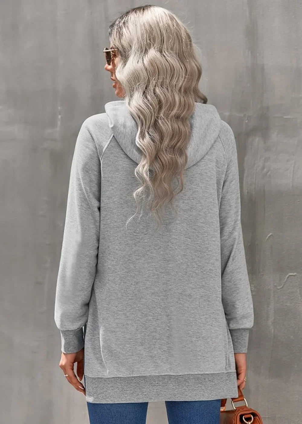Back view of a woman wearing a gray hooded sweatshirt with a long hem and cuffed sleeves.