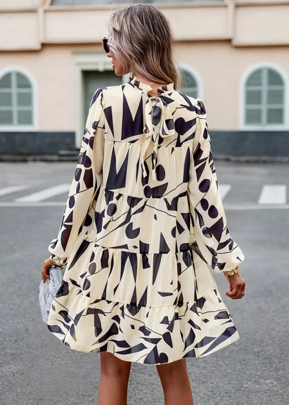 Cream and black abstract print tiered mini dress with long sleeves, shown from the back on a model.