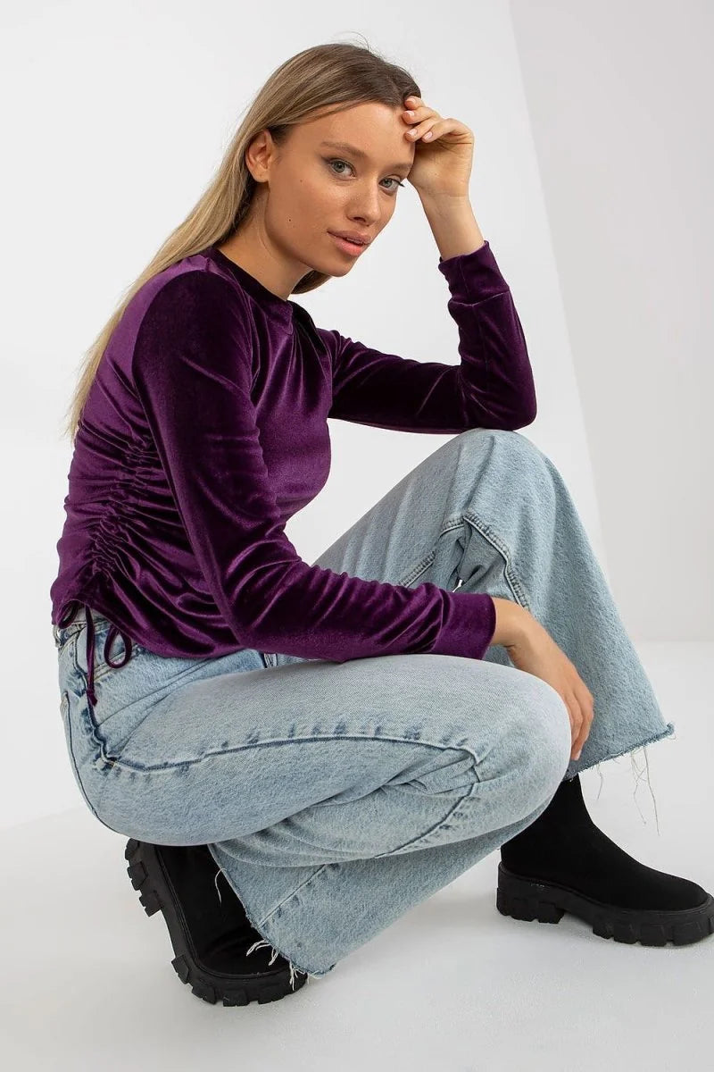 Model in a purple velvet ruched long-sleeve top and light wash wide-leg jeans.