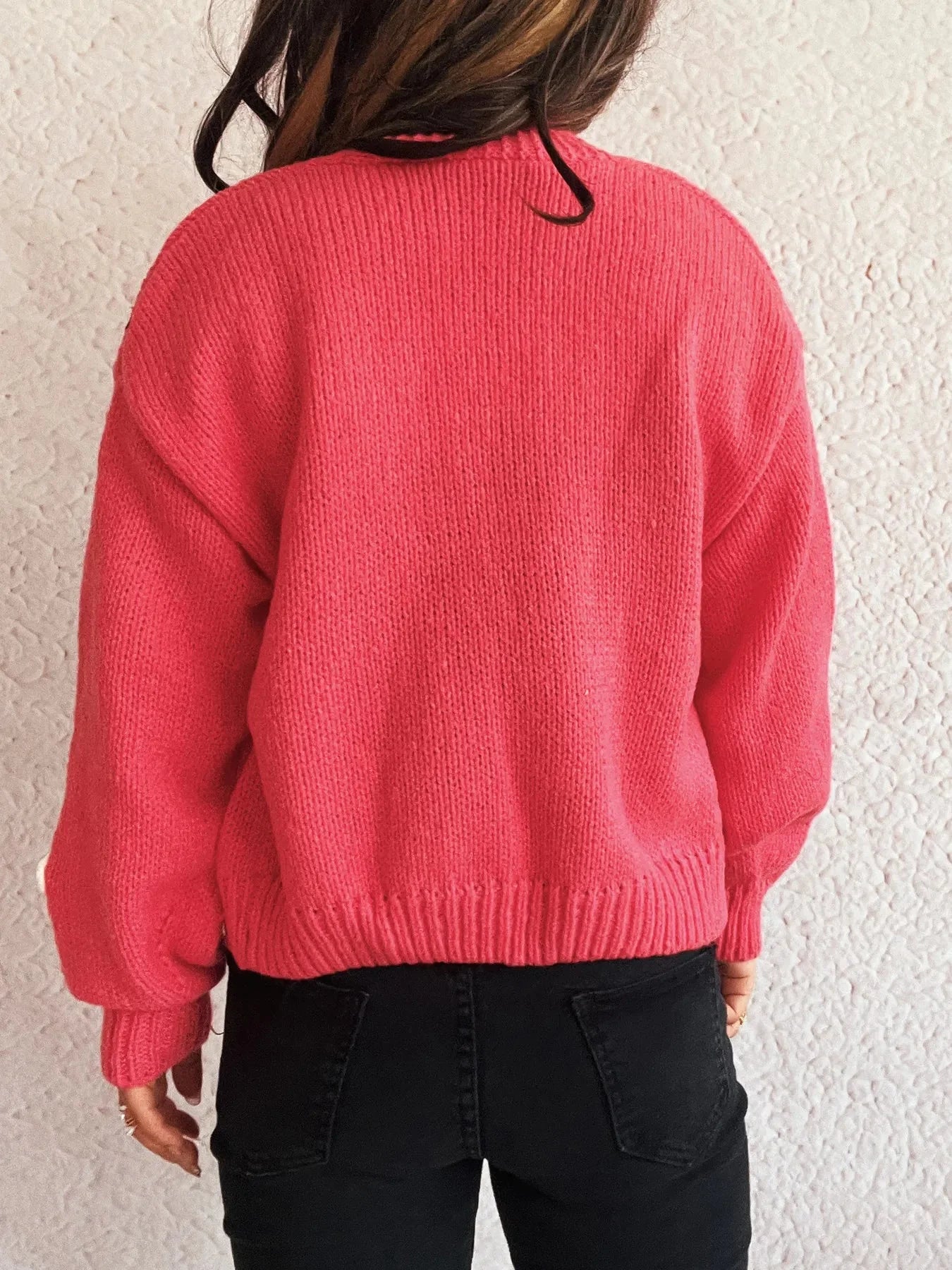Back view of a woman wearing a bright pink knitted sweater and black jeans.