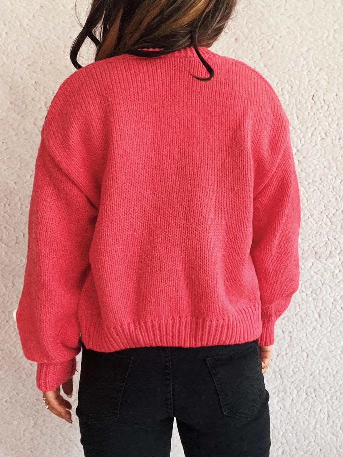 Back view of a woman wearing a bright pink knitted sweater and black jeans.