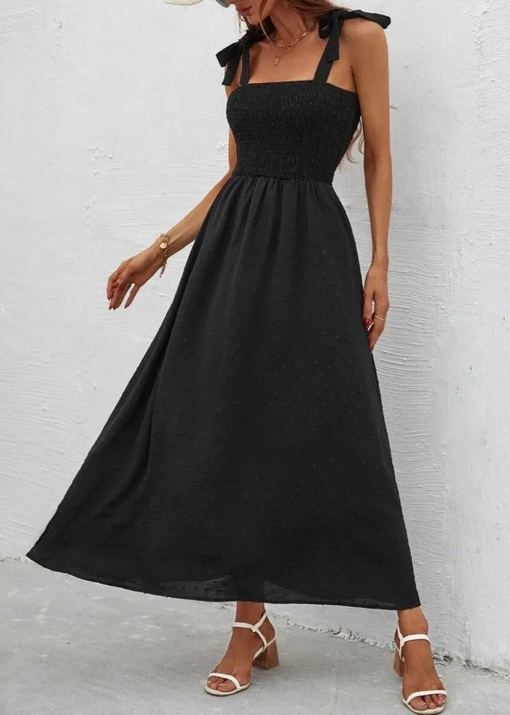 Black smocked bodice midi dress with tie straps and subtle dot pattern, worn by model with white block heel sandals.