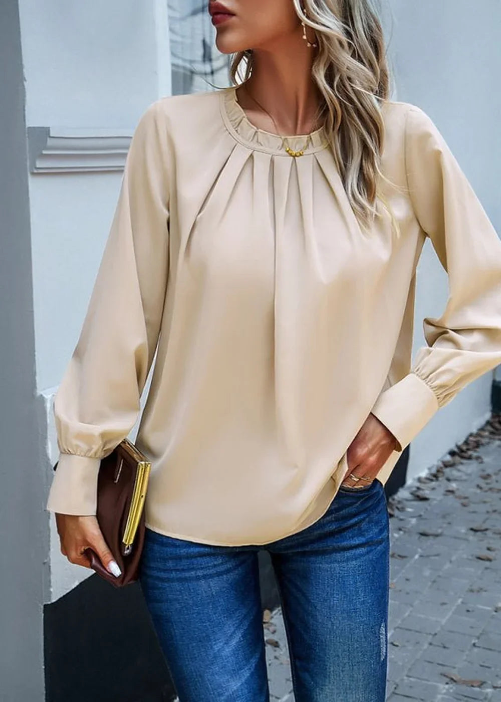 Beige long-sleeve poly blouse with ruffled neckline and cinched cuffs, paired with blue jeans.