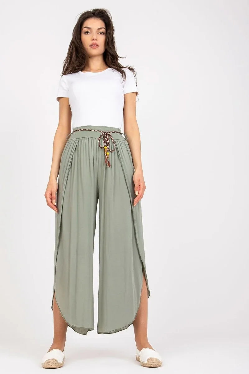 Sage green flowy wide-leg pants with side slits and a braided tasseled belt on a model.