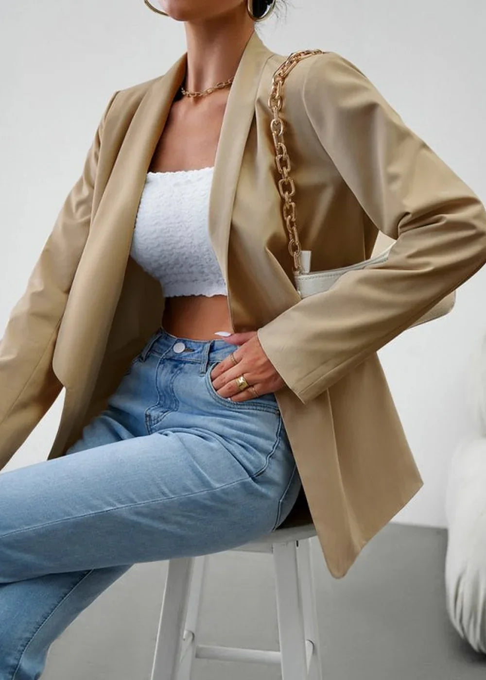 Tan blazer with gold chain detail and white textured top paired with light wash jeans.