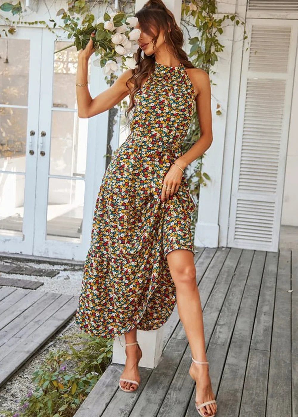 Woman in a floral print halter neck midi dress with a cinched waist, wearing strappy sandals.
